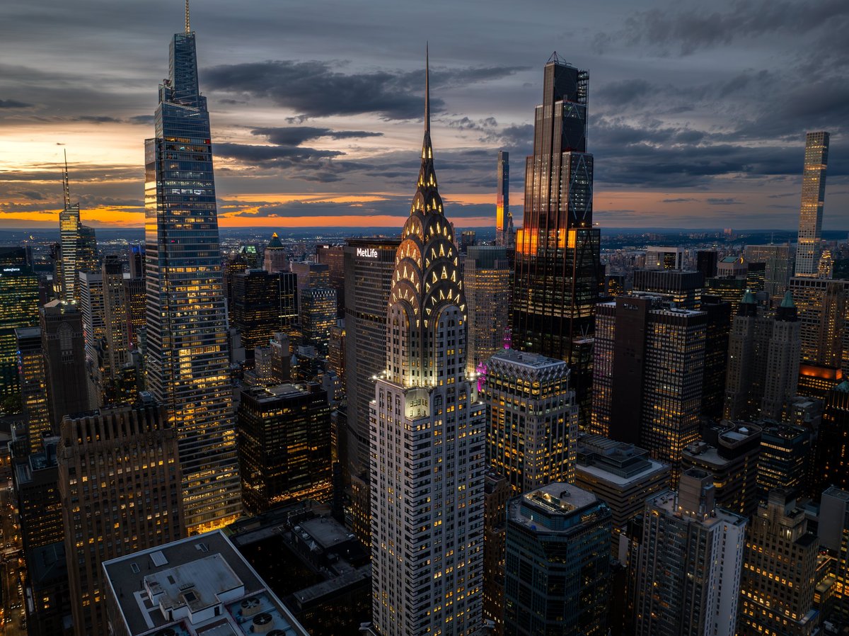 Elevated aerial view of a modern city skyline at dusk with glowing skyscraper lights under a dramatic cloudy sky